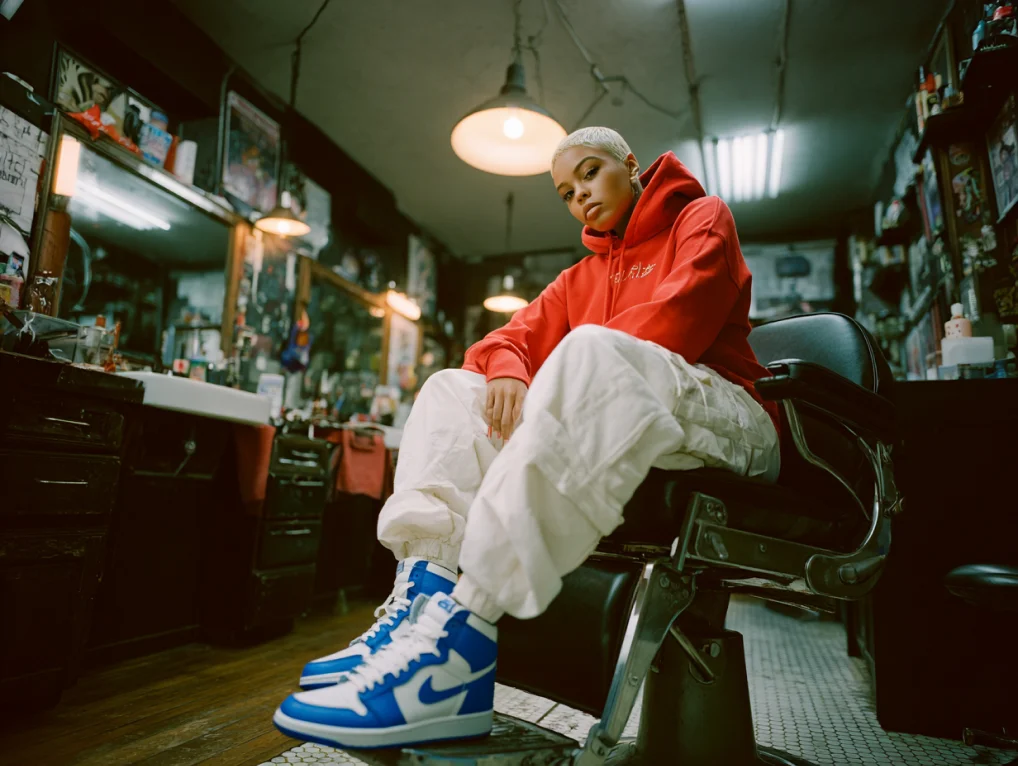 Model in red hoodie and blue sneakers in a barbershop