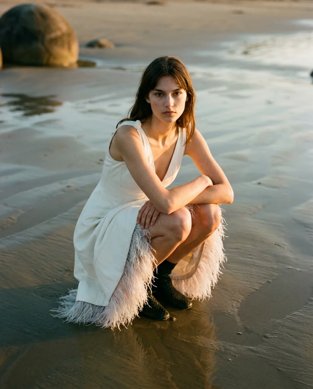 Model crouching on the beach in feathered dress