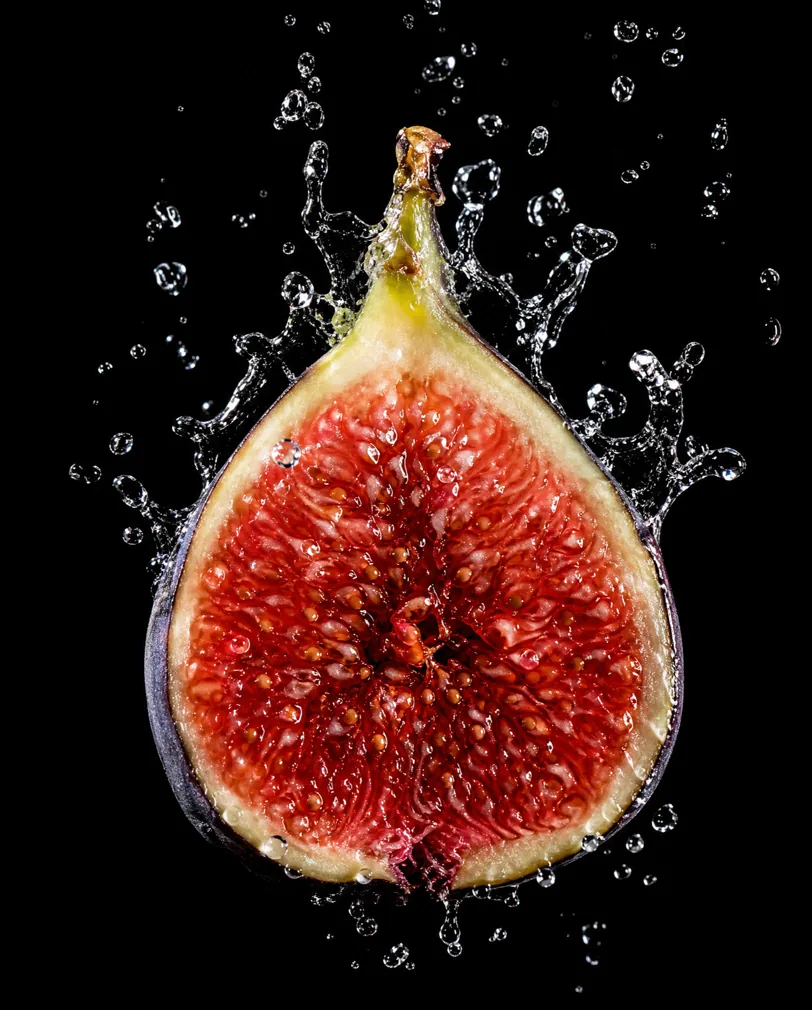 Halved fig in a water splash against black